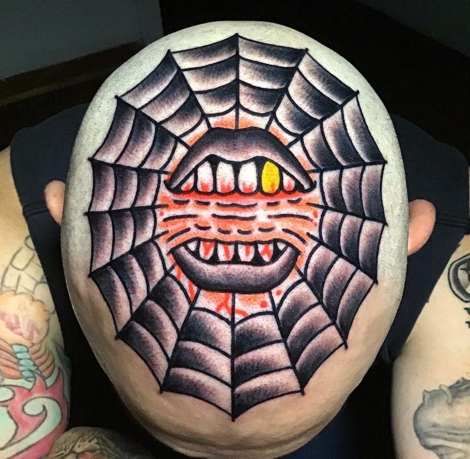 A spiderweb and open mouth tattoo covers the back of a shaved head.