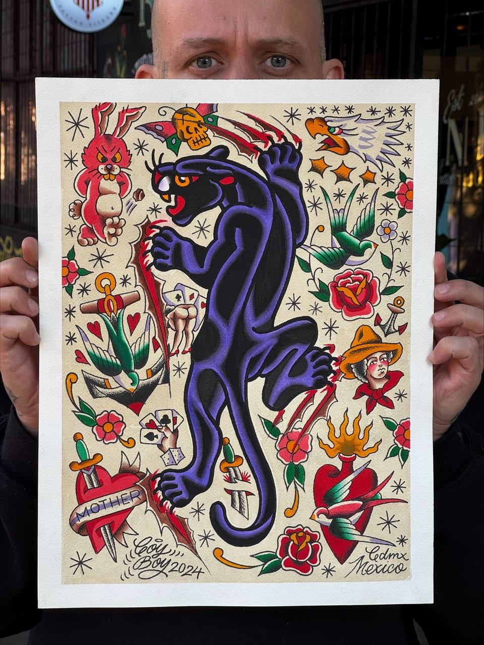 Coy holds a panther flash sheet surrounded by daggers, roses, swallows and other traditional designs.