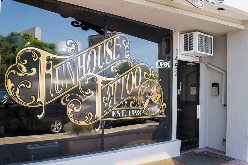 Funhouse Tattoo window lettering and machine emblem from the right, beside the black entry door and a wall air conditioner.