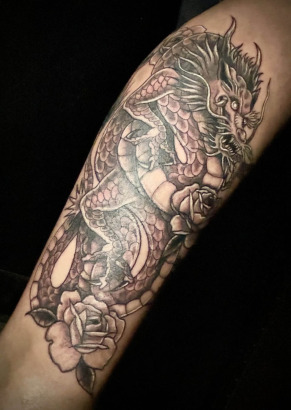 Intricate dragon tattoo with roses on a person's forearm, featuring detailed scales and fierce facial expression.
