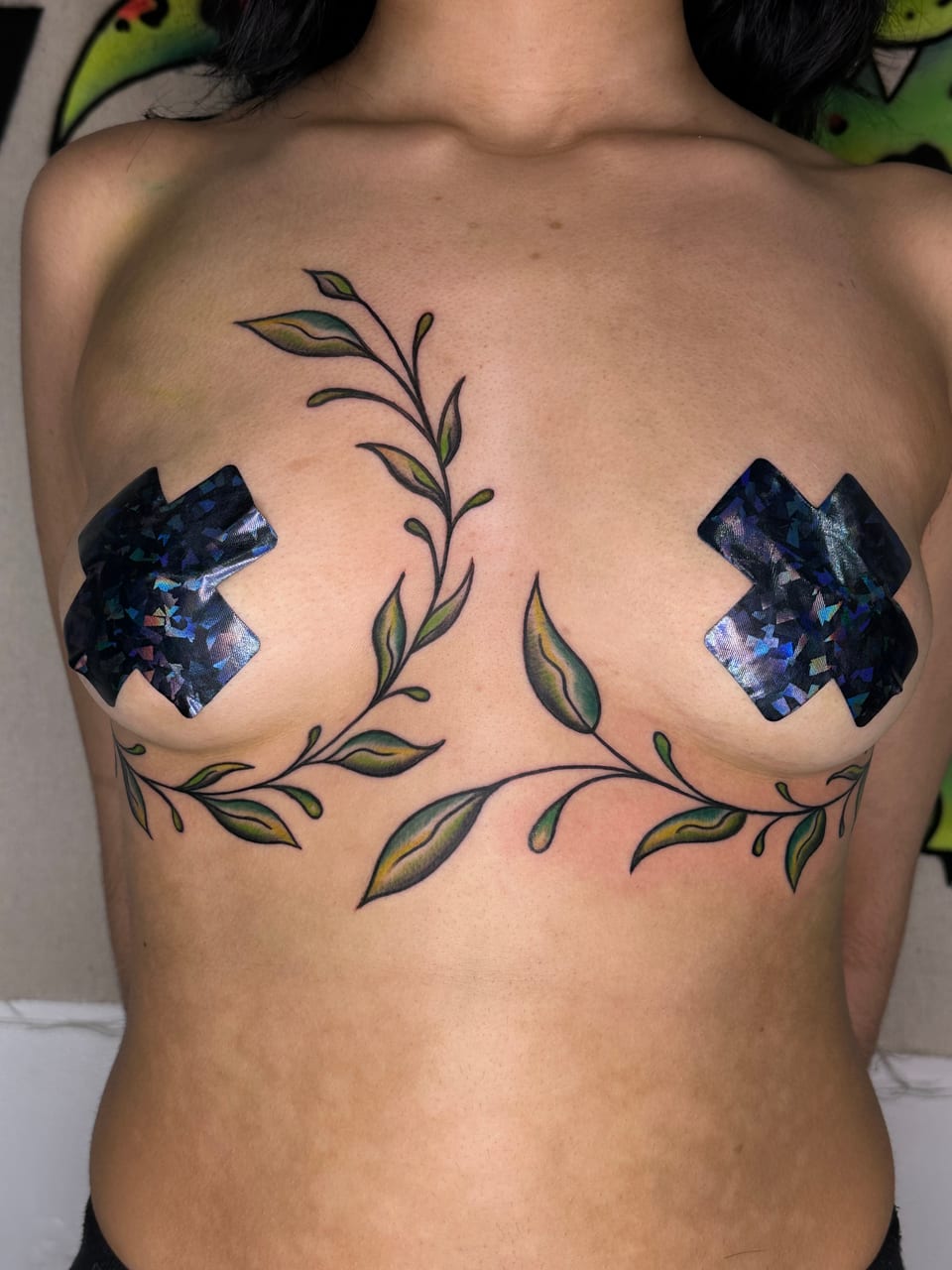 Green and yellow leafy vine tattoos curve around the chest and rise toward the collarbone.