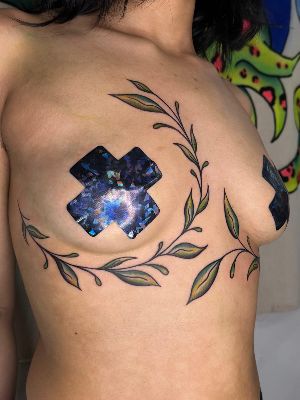 An angled view shows green and yellow leafy vine tattoos curving across the chest.