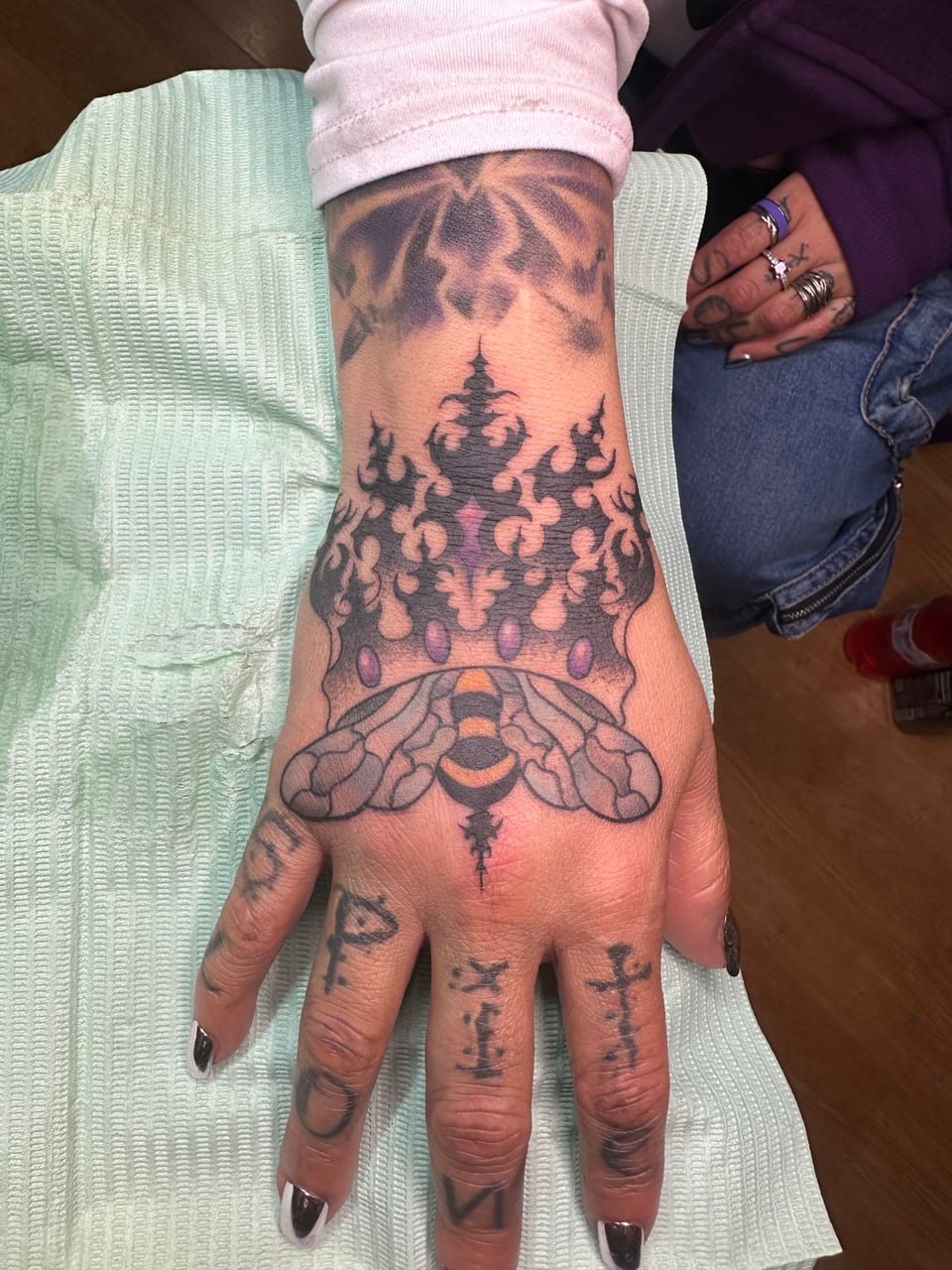 A purple pointed crown and orange insect tattoo covers the back of a hand.