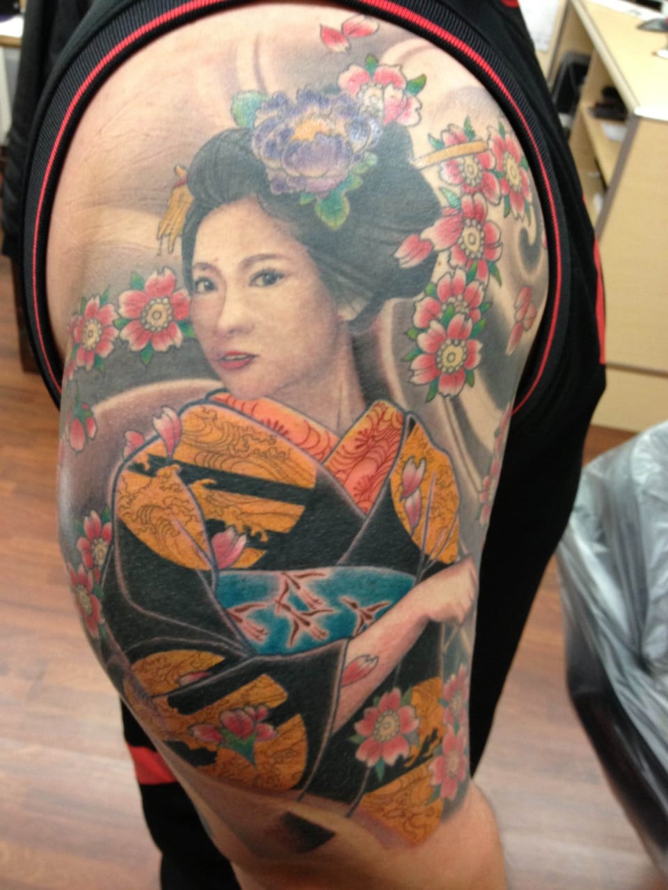 Tattoo of a woman in traditional Japanese attire with flowers and a scenic background.