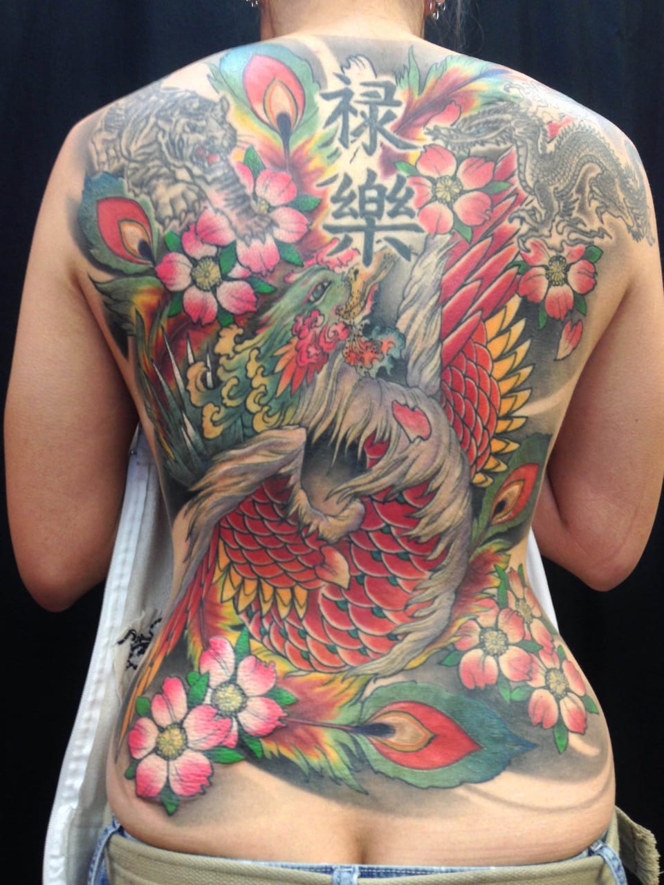 Colorful dragon, pink cherry blossoms, and Japanese characters covering the persons back.