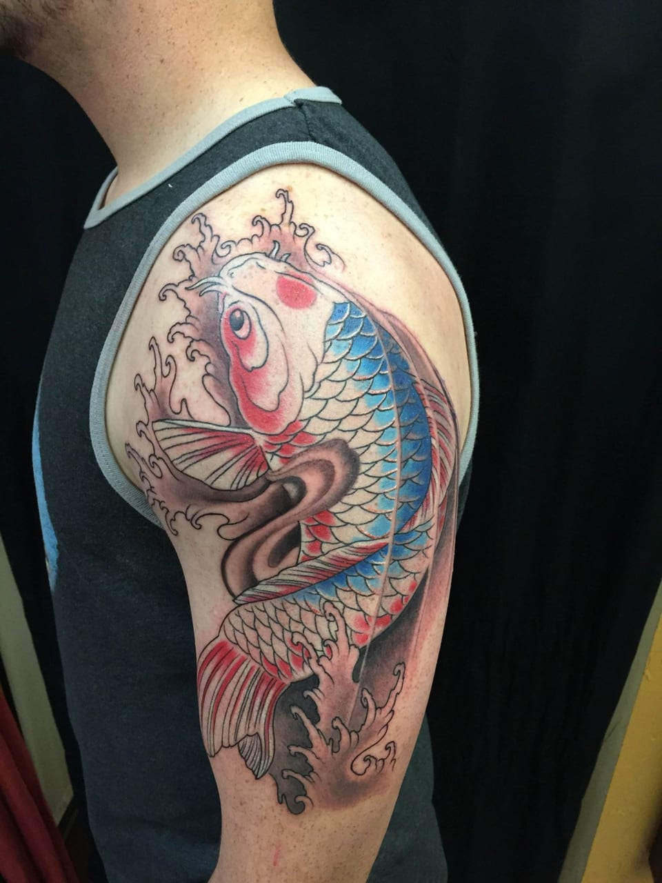 Colorful koi fish tattoo with flowing water on persons upper arm and shoulder.