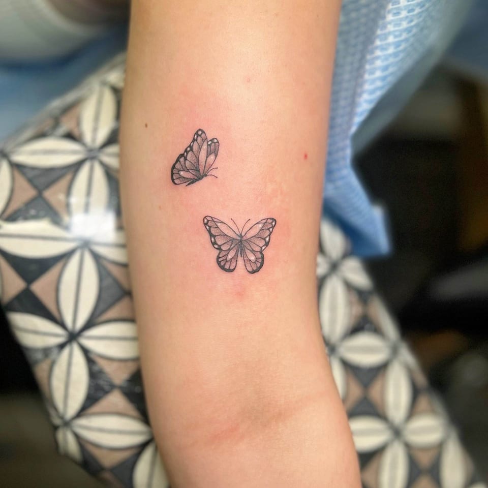 A fine-line black butterfly pair covers an upper arm.