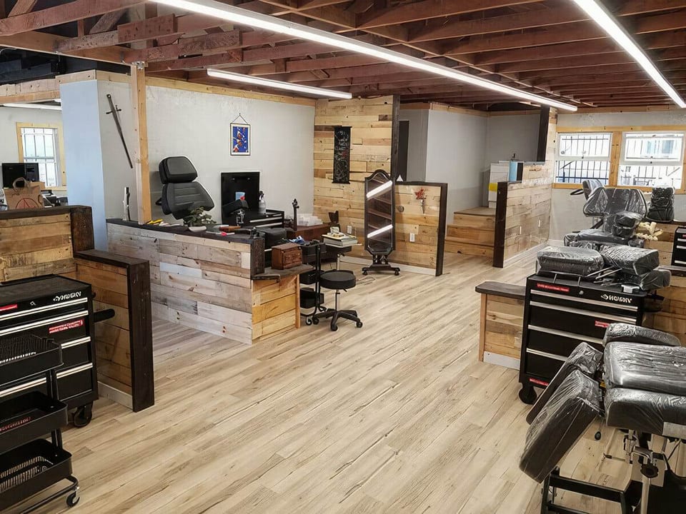 Tattoo chairs and workstations sit between wood-clad counters beneath exposed beams and linear lights.