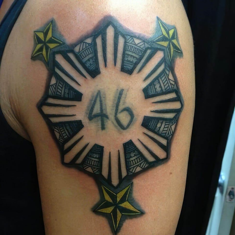 Black Philippine sun with stars and the number 46 tattooed on an upper arm, tattooed by Seth Reynolds