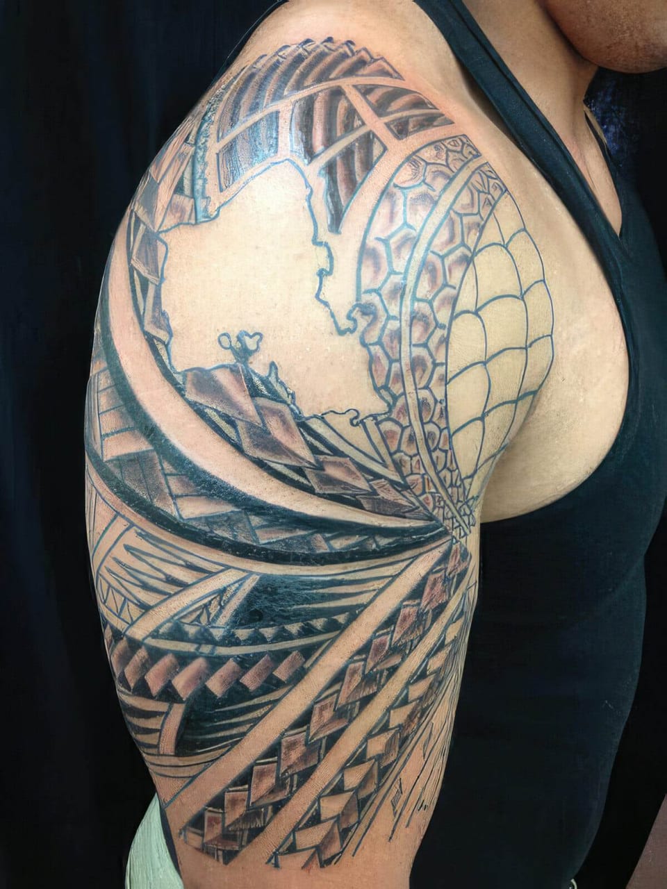 Black Polynesian-style spiderweb and wave pattern tattooed around a shoulder, tattooed by Seth Reynolds