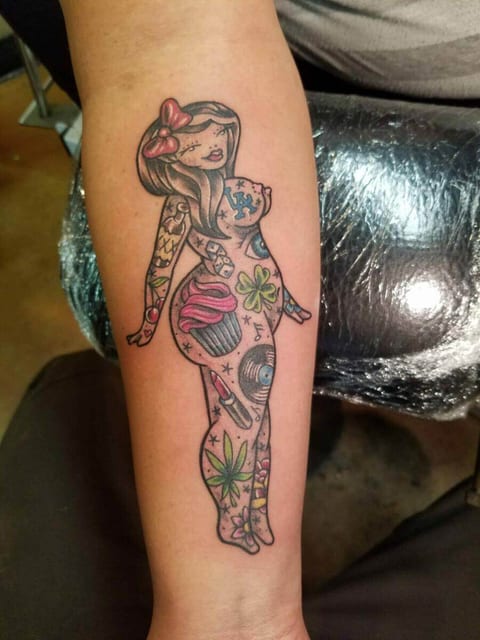 A traditional color tattooed pin-up woman with a red hair bow covers a forearm.
