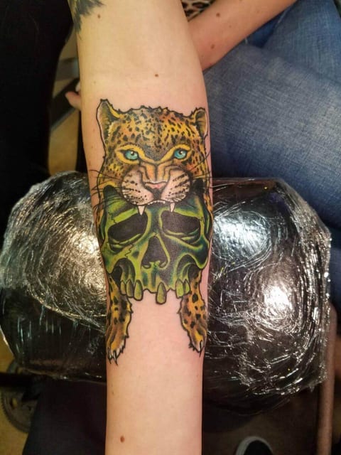 A color illustrative leopard gripping a green skull covers a forearm.