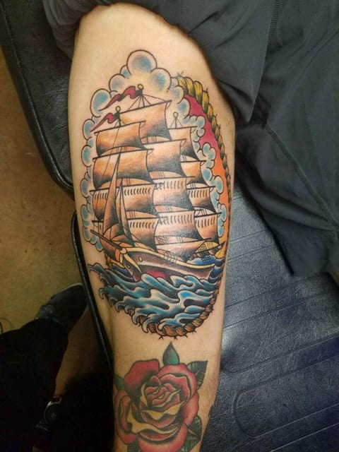 A traditional color sailing ship, rolling blue waves and a rose cover a lower leg.