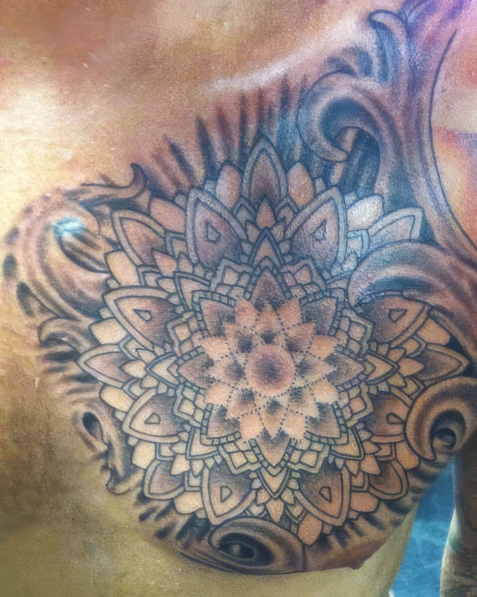 A black and grey ornamental mandala with dotwork petals and shaded scrolls covers the upper chest.