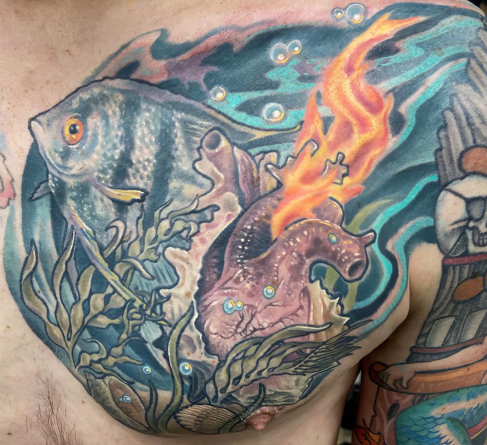 A color illustrative angelfish, seaweed and flaming sea creature cover an upper chest.