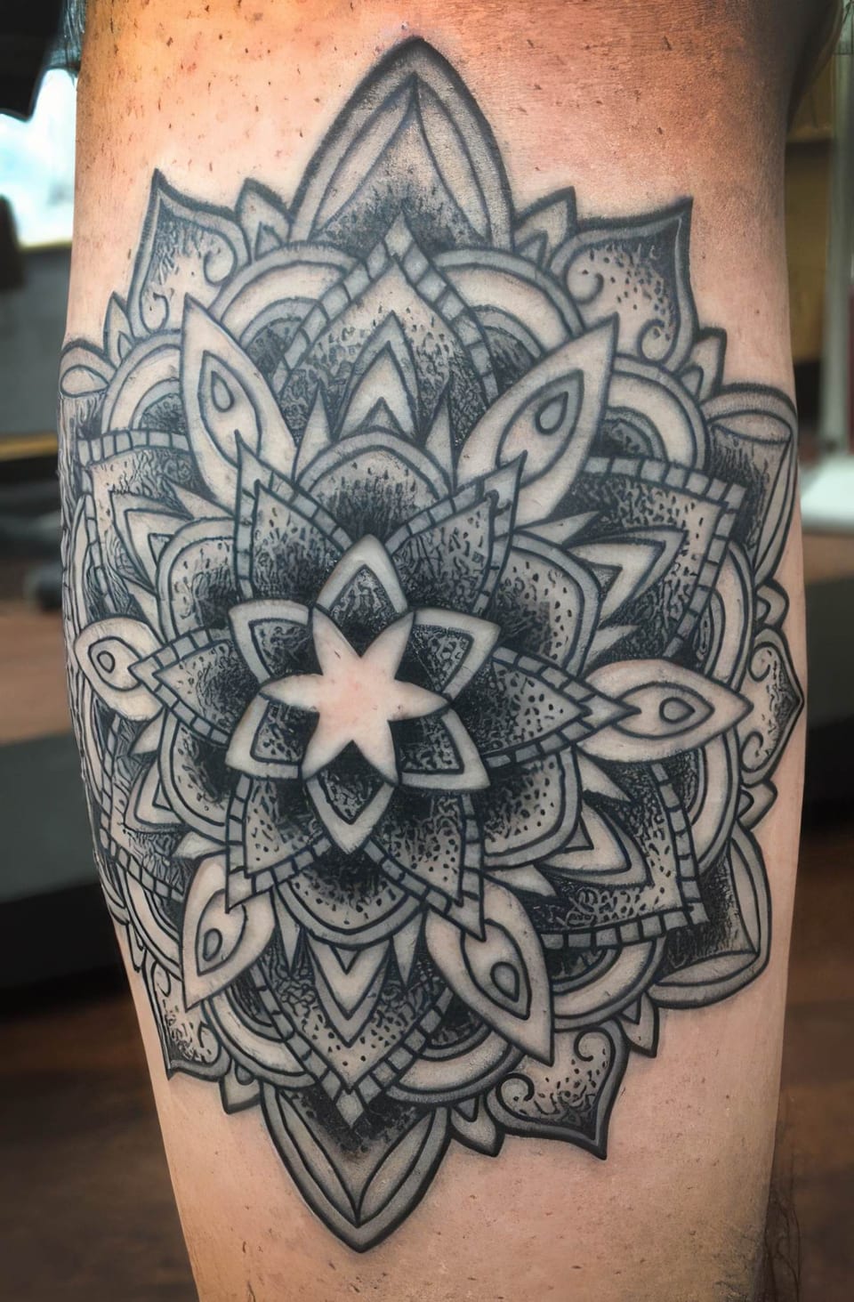 A black dotwork mandala tattoo with layered petals covers a calf.