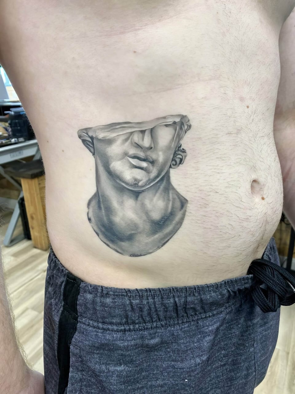 A black and grey realistic broken classical bust covers the side of a stomach.