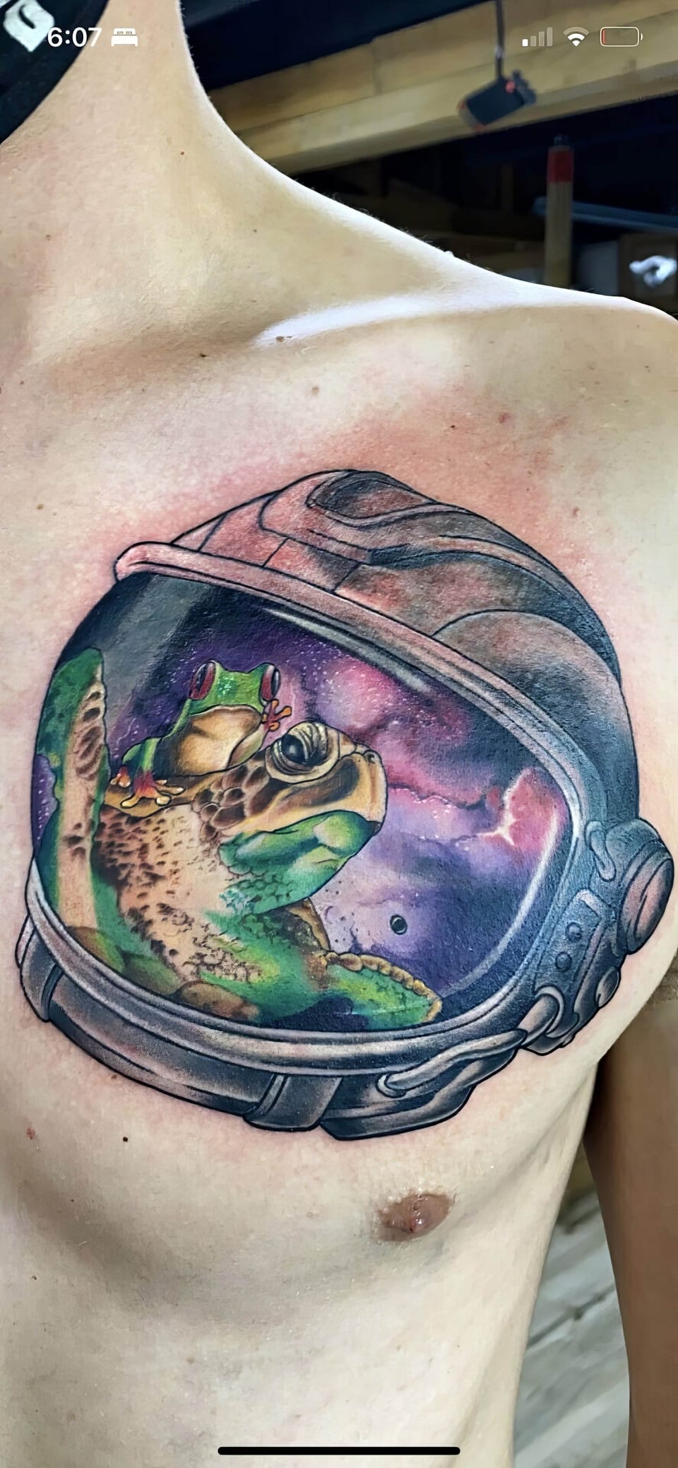 Colorful tattoo of a frog wearing headphones inside a space helmet on persons chest.