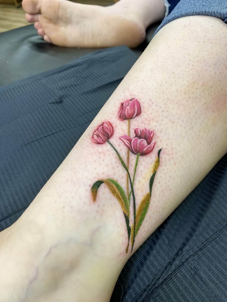 Realistic pink tulips with green stems and leaves cover an inner lower leg.