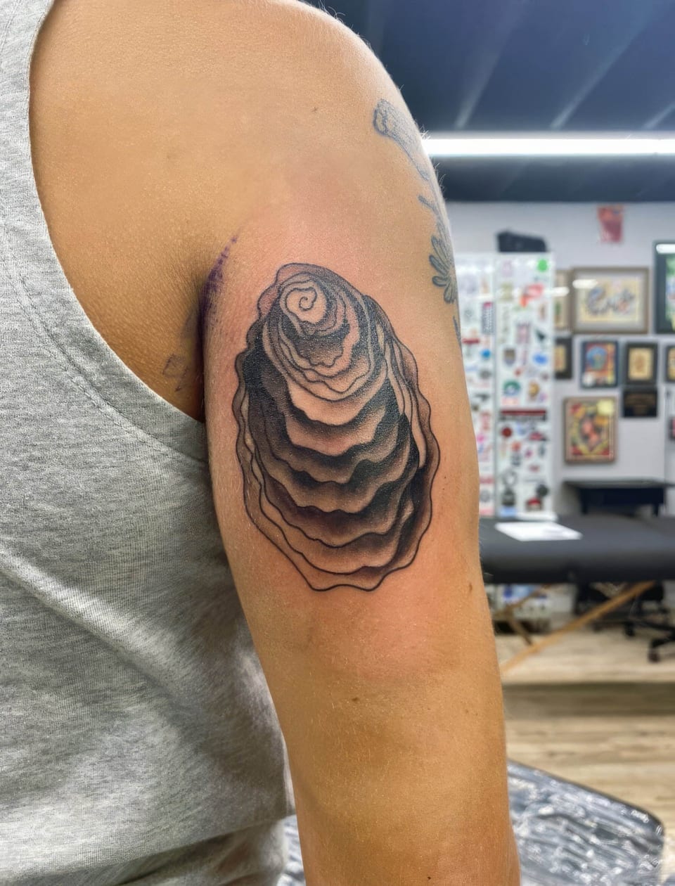 A black and grey illustrative rose with tightly layered petals sits on the back of the upper arm.