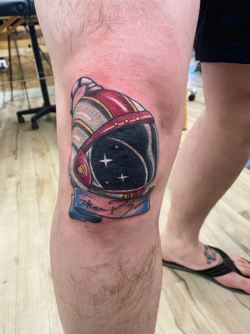 A color illustrative astronaut helmet with stars in its dark visor and a script banner covers the knee.