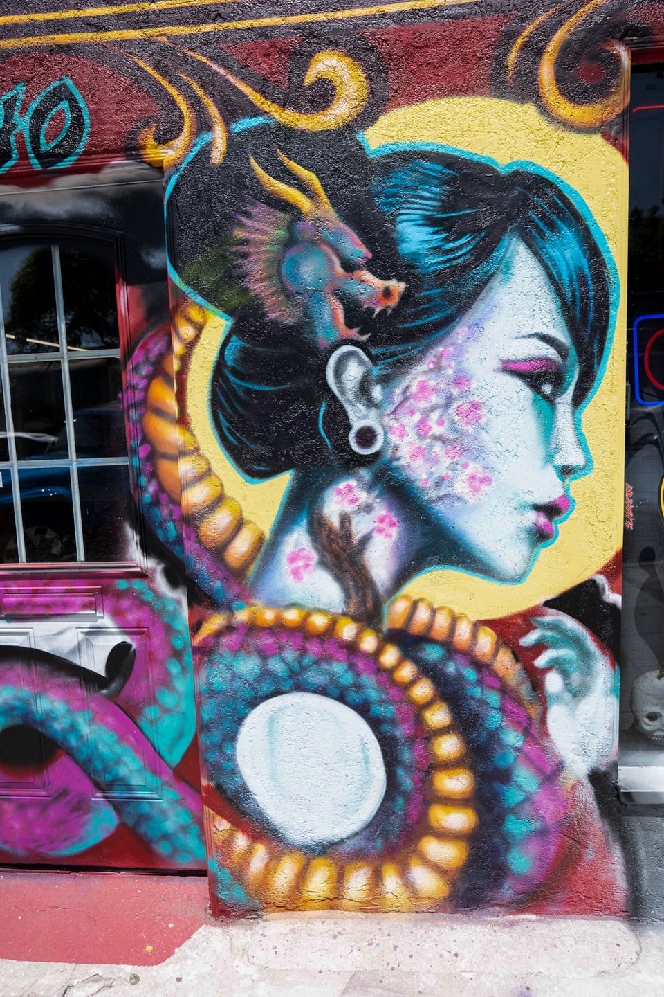 A woman with a dragon hair ornament fills the mural beside a serpent-painted door and neon sign at Redemption Ink.
